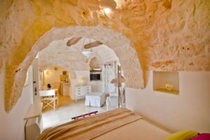 Chambre et salon de la suite avec mur en pierres apparentes Leonardo Trulli Resort Pouilles