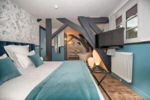 chambre Cuty room couleurs bleu et blanc avec un lit double, salle de bain ouverte sur la chambre et poutres apparentes