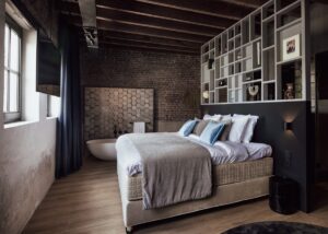 chambre avec baignoire ouverte sur la chambre au style industriel avec la brique apparente sur les murs