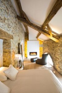 chambre avec mur en pierre apparente, poutre en bois et feu de cheminée