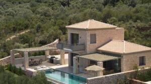 vue de la façade de devant de la maison à louer avec sur la terrasse : transats, salon de jardin avec cheminée, espace repas et barbecue