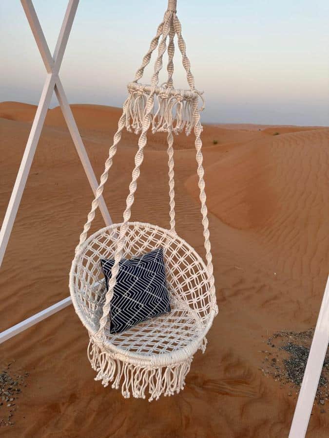 fauteuil balancelle en macramé au milieu des dunes de sable du désert