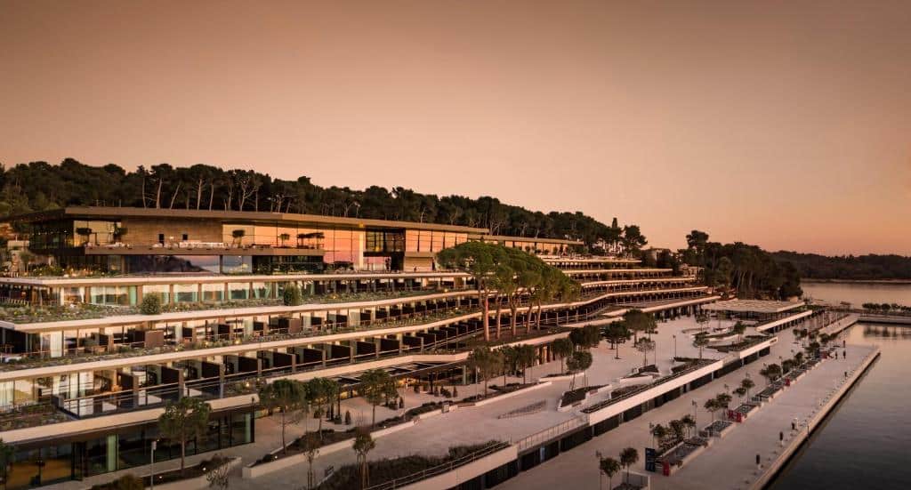 façade de l'hôtel Grand park Hotel Rovinj face à la marina de la ville avec une grande esplanade pour se promener et une galerie commerçante