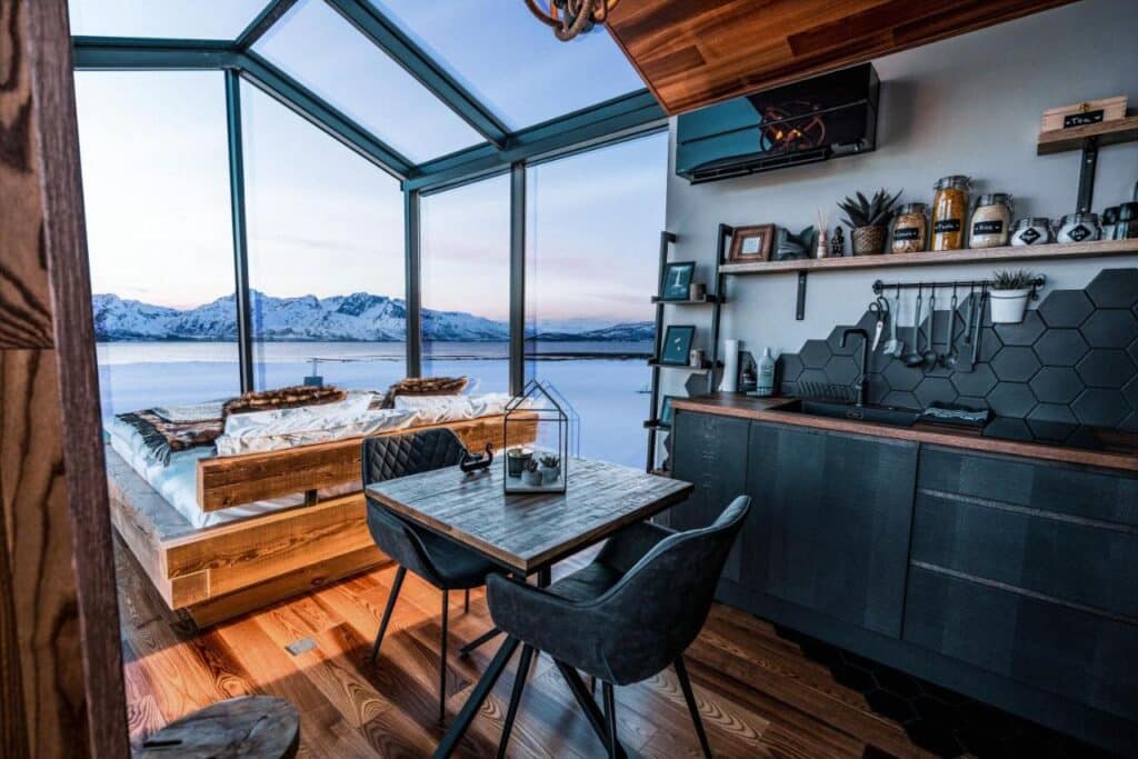 intérieur d'un Panorama Glass Lodge avec une partie chambre, une kitchenette et un espace repas où le petit déjeuner est livré le matin